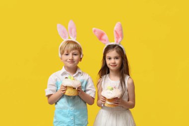 Sarı arka planda Paskalya pastaları olan tavşan kulaklı şirin çocuklar.