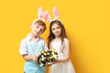 Sarı arka planda Paskalya çelengi olan tavşan kulaklı şirin çocuklar.