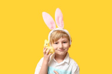 Sarı arka planda Paskalya tavşanı olan tavşan kulaklı şirin bir çocuk.