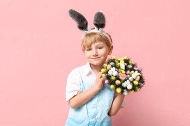 Pembe arka planda Paskalya çelengi olan tavşan kulaklı şirin bir çocuk.