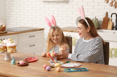 Sevimli küçük kız ve annesi mutfakta Paskalya yumurtası boyuyor.