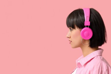 Pembe arka planda burun piercingli, kulaklıklı şık genç bir kadın.