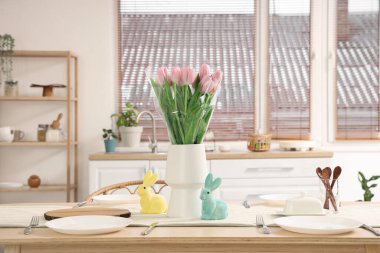 Mutfaktaki yemek masasında vazo, lale ve Paskalya tavşanı.