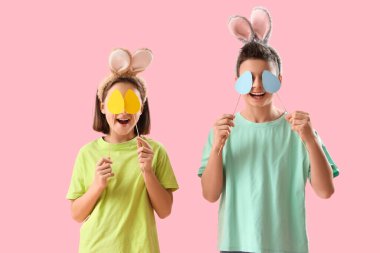 Tavşan kulaklı mutlu çocuklar, pembe arka planda kağıt Paskalya yumurtaları.