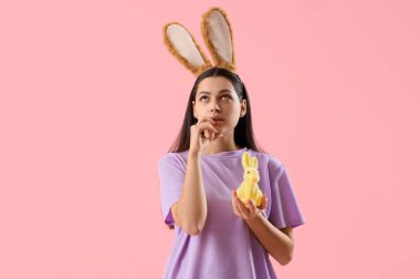 Tavşan kulaklı düşünceli genç bir kadın ve pembe arka planda Paskalya tavşanı.