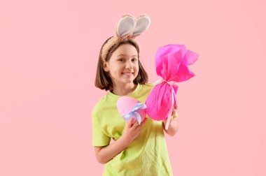Tavşan kulaklı küçük kız, pembe arka planda Paskalya hediyesi yumurtaları.