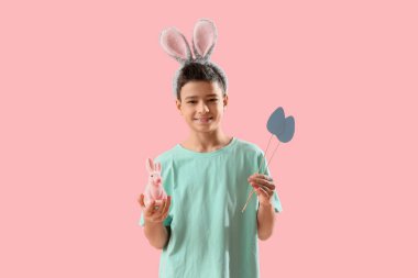 Paskalya tavşanı ve pembe arka planda kağıttan yumurtaları olan tavşan kulaklı küçük çocuk.