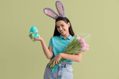 Paskalya yumurtası ve yeşil arka planda laleleri olan tavşan kulaklı genç bir kadın.