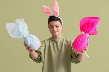 Yeşil arka planda Paskalya hediyesi yumurtaları olan tavşan kulaklı küçük çocuk.