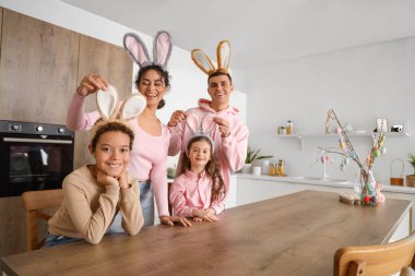Paskalya günü mutfaktaki masada tavşan kulaklı mutlu bir aile.