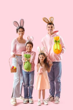 Pembe arka planda Paskalya yumurtaları olan tavşan kulaklı mutlu bir aile.