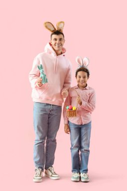 Pembe arka planda Paskalya yumurtaları olan tavşan kulaklı küçük çocuk ve babası