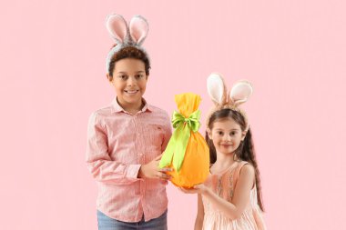 Pembe arka planda Paskalya hediyesi yumurtası olan tavşan kulaklı çocuklar.