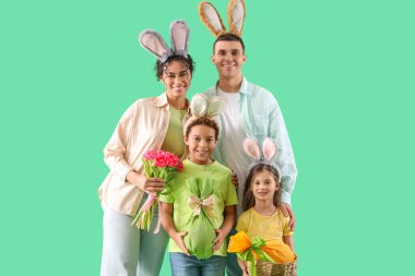 Paskalya hediyesi yumurta ve yeşil arka planda laleleri olan tavşan kulaklı mutlu bir aile.