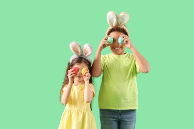 Yeşil arka planda Paskalya yumurtaları olan tavşan kulaklı küçük çocuklar.