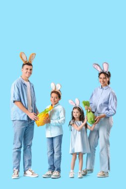 Mavi arka planda Paskalya hediyesi yumurtaları olan tavşan kulaklı mutlu bir aile.