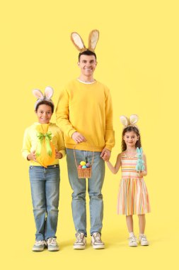 Babalarıyla küçük çocuklar ve sarı arka planda Paskalya yumurtaları.