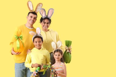 Tavşan kulaklı mutlu bir aile Paskalya çelengi ve sarı arka planda hediye yumurtaları.