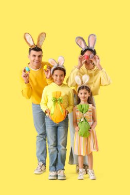 Sarı arka planda Paskalya yumurtaları olan tavşan kulaklı mutlu bir aile.