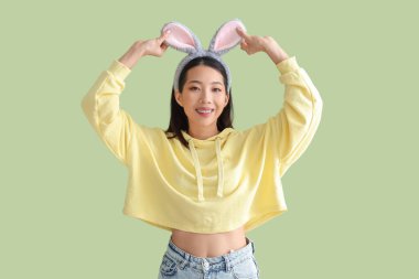 Yeşil arka planda tavşan kulaklı genç Asyalı kadın. Paskalya kutlaması