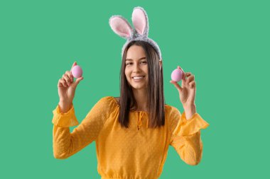 Yeşil arka planda Paskalya yumurtaları olan tavşan kulaklı genç bir kadın.