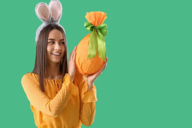 Yeşil arka planda Paskalya hediyesi yumurtası olan tavşan kulaklı genç bir kadın.