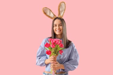 Pembe arka planda laleleri olan tavşan kulaklı genç bir kadın. Paskalya kutlaması