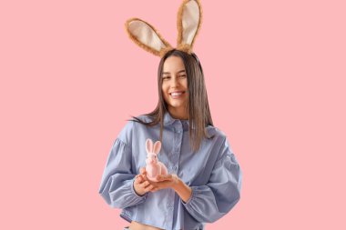 Pembe arka planda Paskalya tavşanı olan tavşan kulaklı genç bir kadın.