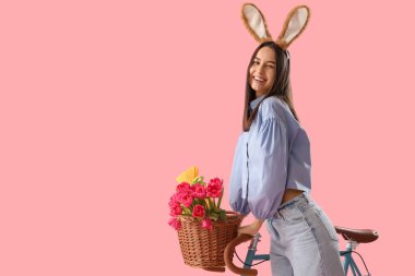 Pembe arka planda bisikleti olan tavşan kulaklı genç bir kadın. Paskalya kutlaması