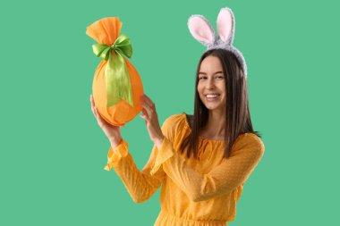 Yeşil arka planda Paskalya hediyesi yumurtası olan tavşan kulaklı genç bir kadın.