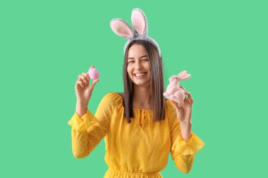 Tavşan kulaklı genç bir kadın. Yeşil arka planda Paskalya tavşanı ve yumurtası var.