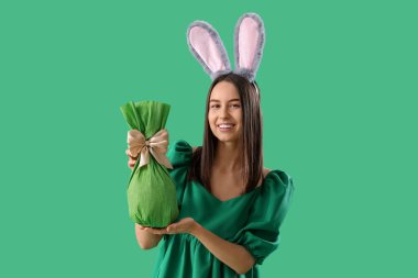 Yeşil arka planda Paskalya hediyesi yumurtası olan tavşan kulaklı genç bir kadın.