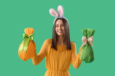 Yeşil arka planda Paskalya hediyesi yumurtaları olan tavşan kulaklı genç bir kadın.