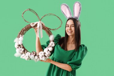 Yeşil arka planda Paskalya çelengi olan tavşan kulaklı genç bir kadın.