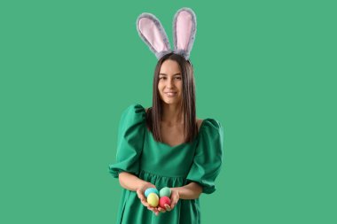 Yeşil arka planda Paskalya yumurtaları olan tavşan kulaklı genç bir kadın.