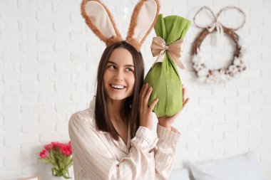 Tavşan kulaklı genç bir kadın ve yatak odasında Paskalya hediyesi yumurtası.