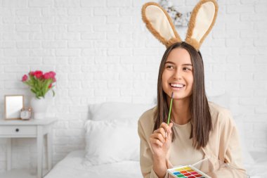 Tavşan kulaklı düşünceli genç kadın yatak odasında paskalya yumurtası boyuyor.