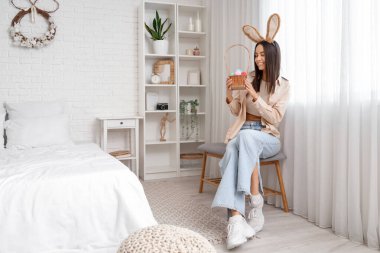 Tavşan kulaklı genç bir kadın ve yatak odasında paskalya yumurtası sepeti.