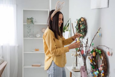 Tavşan kulaklı, söğüt dallarını evde paskalya yumurtasıyla süsleyen genç bir kadın.