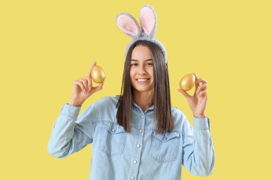 Sarı arka planda Paskalya yumurtaları olan tavşan kulaklı genç bir kadın.