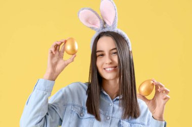 Sarı arka planda Paskalya yumurtaları olan tavşan kulaklı genç kadın, yakın plan.