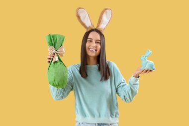 Tavşan kulaklı, Paskalya tavşanı ve sarı arka planda hediye yumurtası olan genç bir kadın.