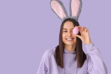 Leylak arka planında Paskalya yumurtası olan tavşan kulaklı genç bir kadın.