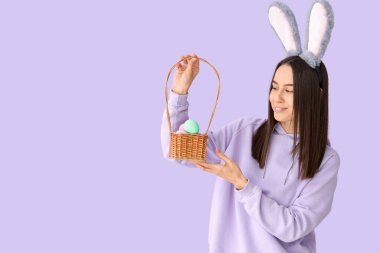 Leylak arka planında Paskalya yumurtaları olan tavşan kulaklı genç bir kadın.