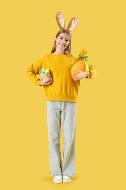 Sarı arka planda Paskalya yumurtaları olan tavşan kulaklı genç bir kadın.