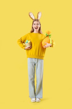 Sarı arka planda Paskalya yumurtaları olan tavşan kulaklı genç bir kadın.