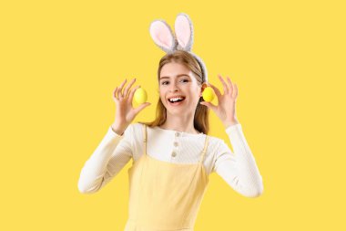 Sarı arka planda Paskalya yumurtaları olan tavşan kulaklı genç bir kadın.