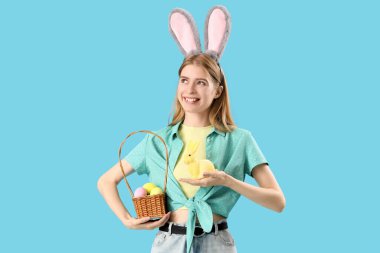Tavşan kulaklı genç bir kadın. Mavi arka planda Paskalya tavşanı ve yumurtaları var.