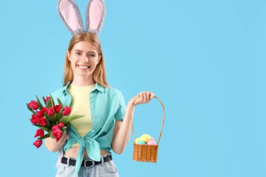 Mavi arka planda lale ve Paskalya yumurtaları olan tavşan kulaklı genç bir kadın.