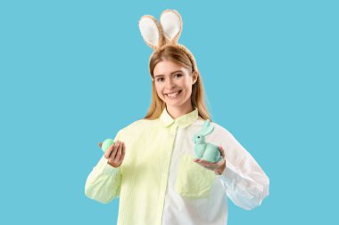 Tavşan kulaklı genç bir kadın. Mavi arka planda Paskalya tavşanı ve yumurtaları var.